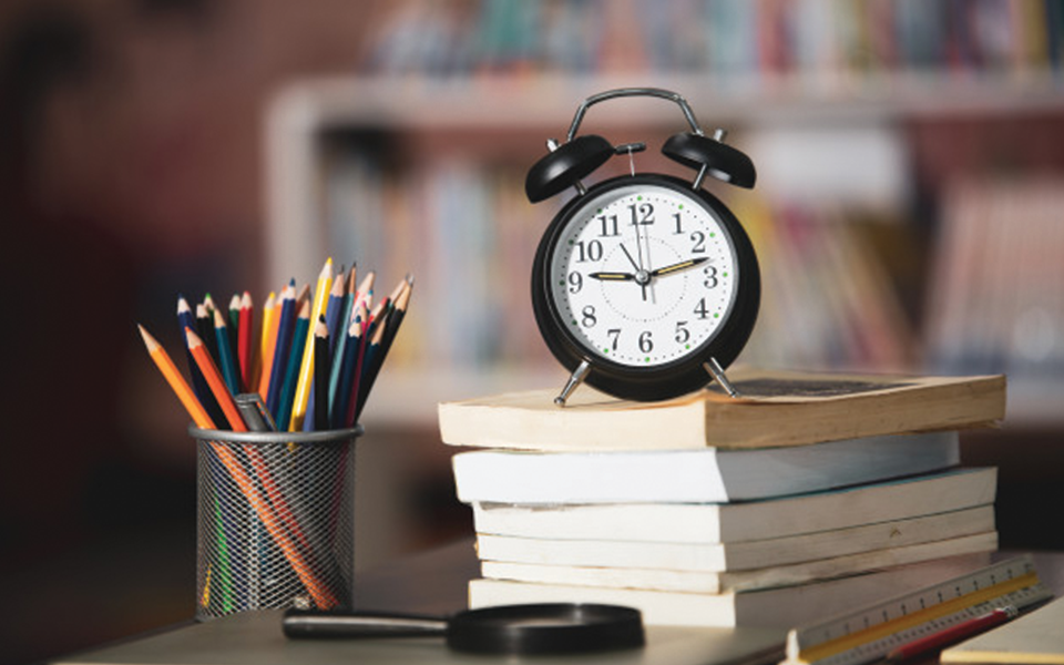 Desk setup with alarm clock and school supplies, preparing for college decision waiting period, The Red Pen
