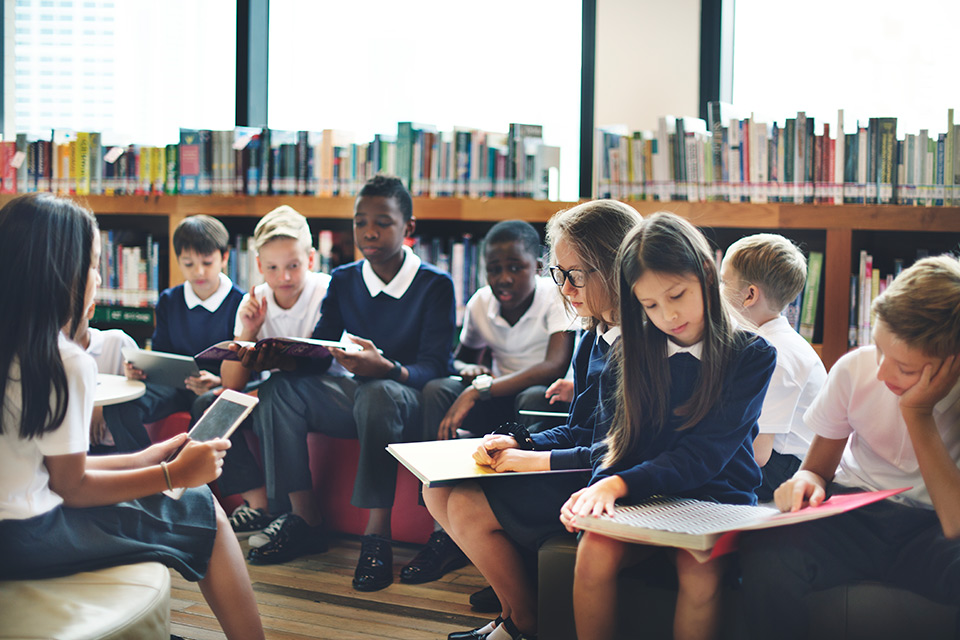 Children reading and discussing in a school library, symbolizing early education at global boarding schools by The Red Pen