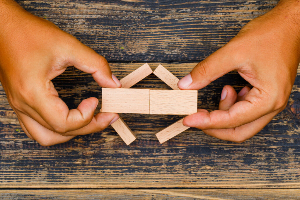 Hands carefully assembling wooden blocks on a vintage wooden surface, representing the blending of liberal arts and STEM - The Red Pen