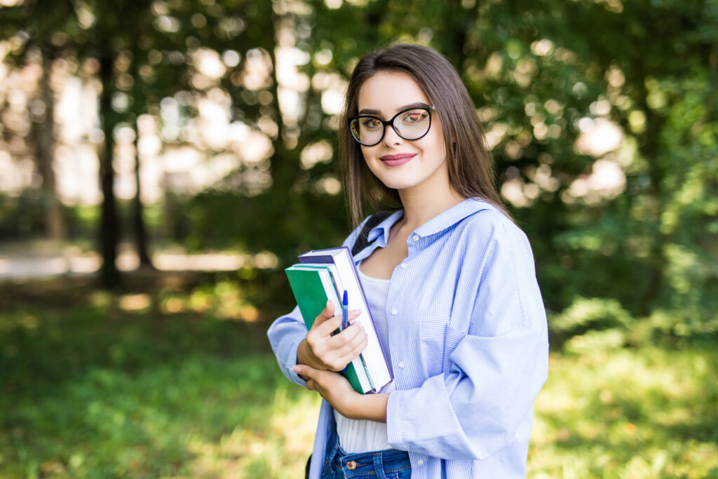College student holding books in a lush green park, understanding demonstrated interest in college admissions by The Red Pen