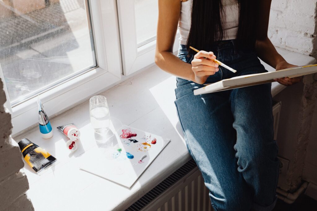 Young artist painting on a canvas by a sunny window, illustrating portfolio creation tips by The Red Pen