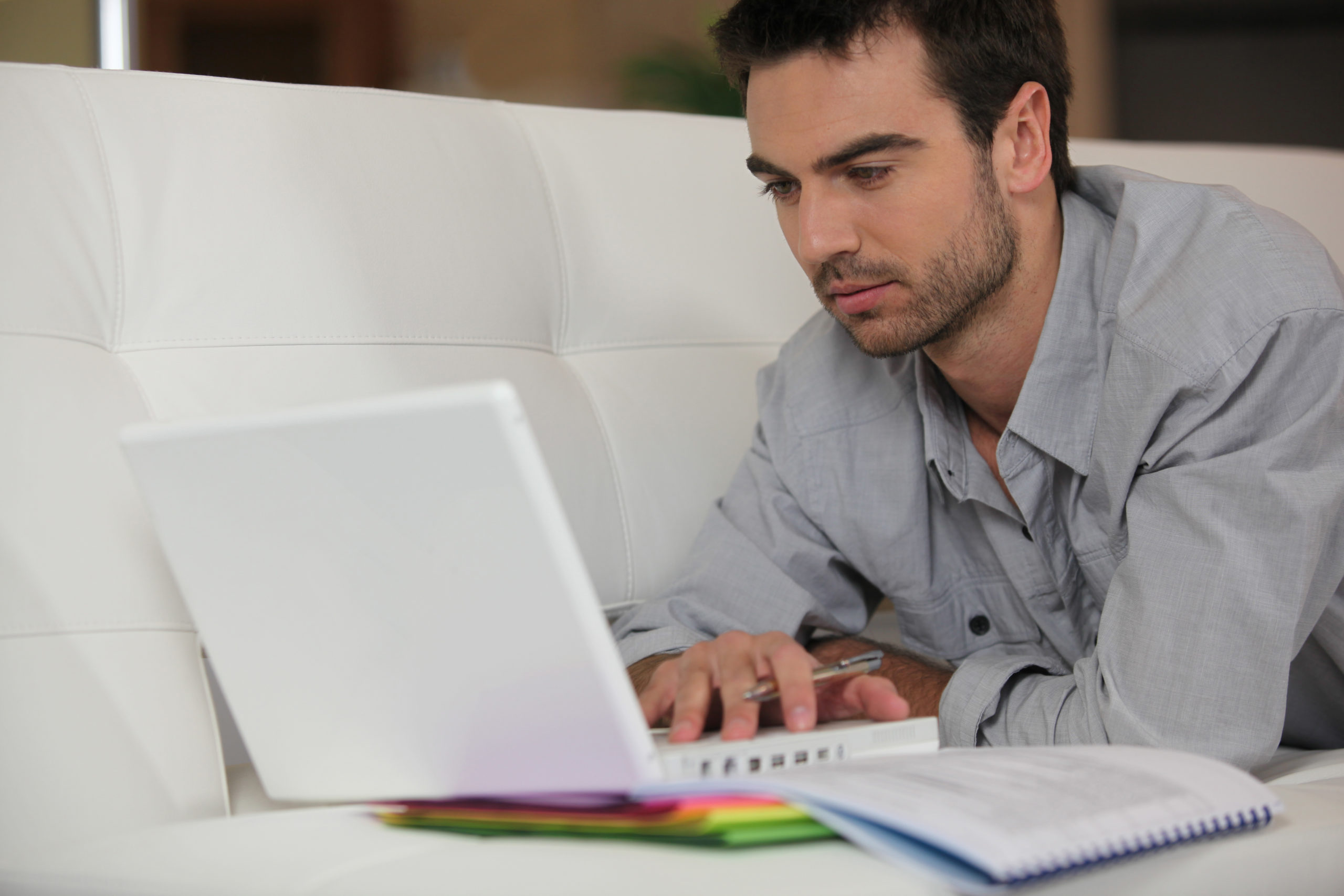 Person using a laptop on a couch with notebooks and colorful folders, representing the importance of UX – UX is Not Extra | The Red Pen