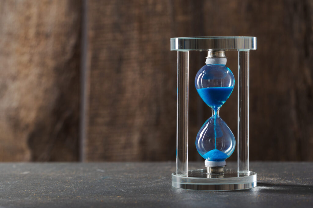 Blue sand flowing in an hourglass, reflecting the concept of time and extended deadlines in MBA applications – COVID-19 Effects: Extended MBA Deadlines and New Rounds | The Red Pen