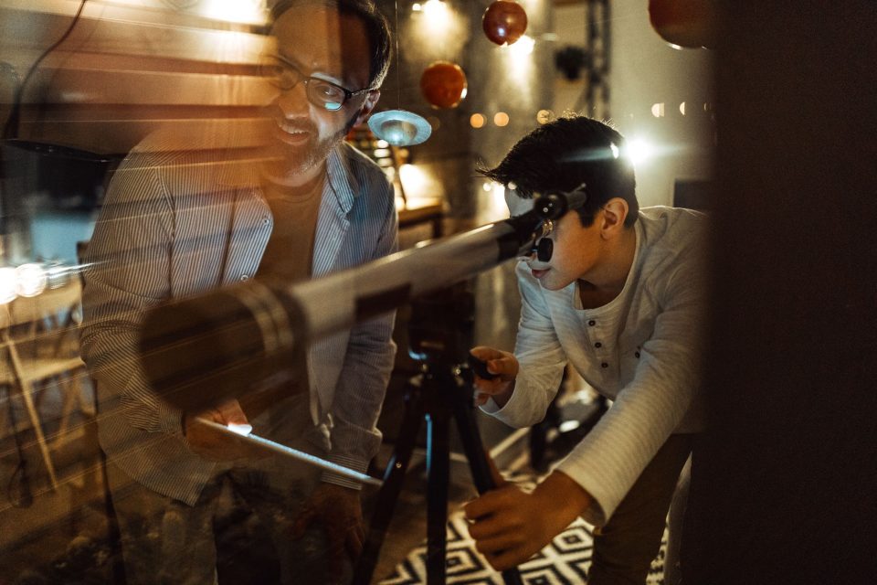 Parent and child exploring the universe with a telescope, symbolizing the importance of research and academic growth – Benefits of Credit Courses and Research Papers for High School Students | The Red Pen