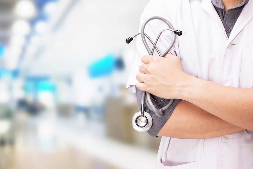 Healthcare worker holding a stethoscope with blurred hospital corridor by The Red Pen
