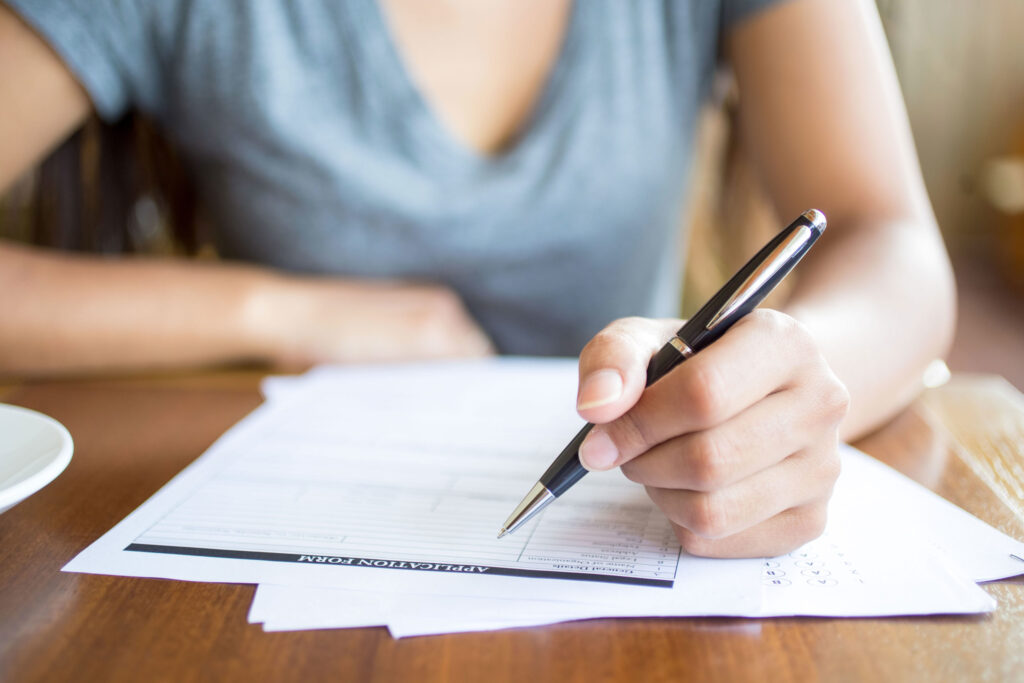 Close-up of hands writing on application paperwork, addressing early application myths - The Red Pen