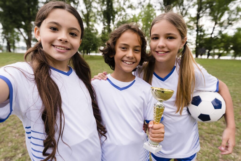 Three girls in soccer uniforms holding a trophy in a park, representing benefits of single-gender education, The Red Pen