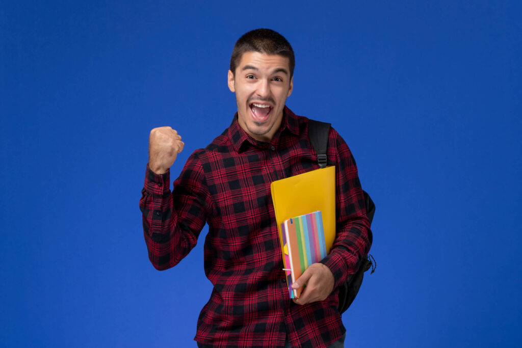 Smiling man holding colorful notebooks and giving a victorious fist pump, symbolizing success in graduate school applications – 5 Secrets to Acing Applications for Top Graduate Schools | The Red Pen