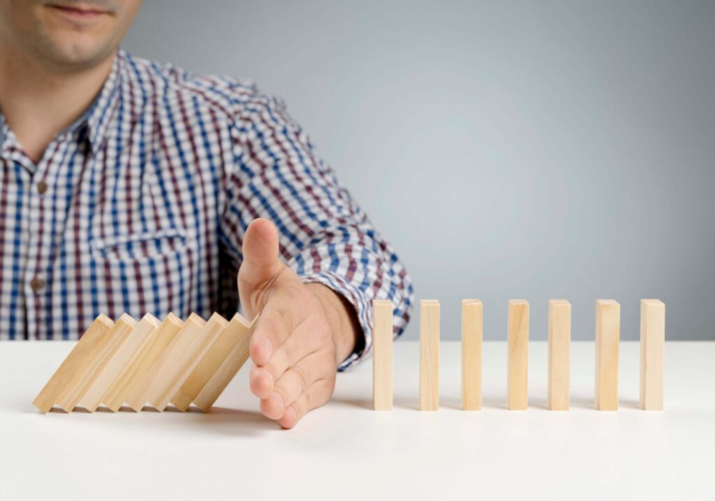 Hand preventing dominoes from falling, representing common mistakes to avoid in postgraduate applications – The Red Pen