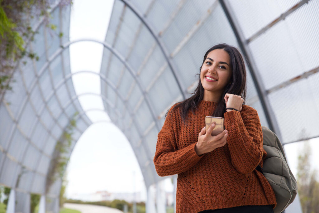 Young woman in a cozy sweater with a backpack, showing enthusiasm for college applications and demonstrated interest - The Red Pen