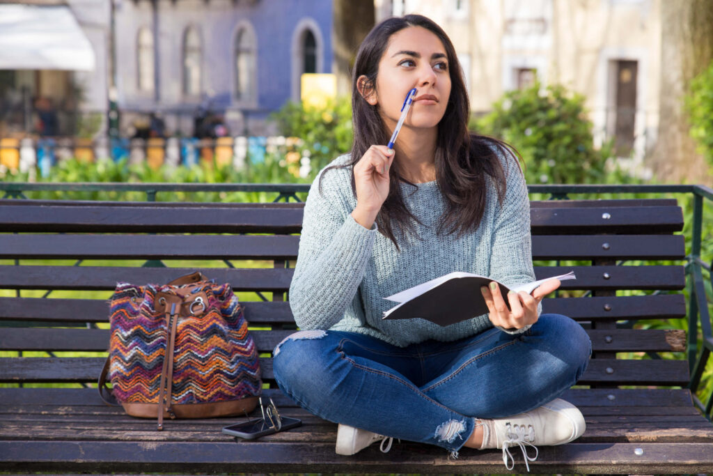 Young woman brainstorming ideas for her college application essay outdoors - The Red Pen
