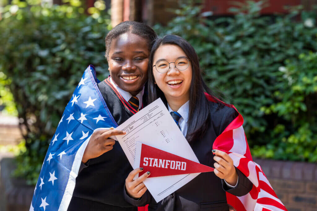 International high school graduates holding Stanford pennant and American flag, The Red Pen